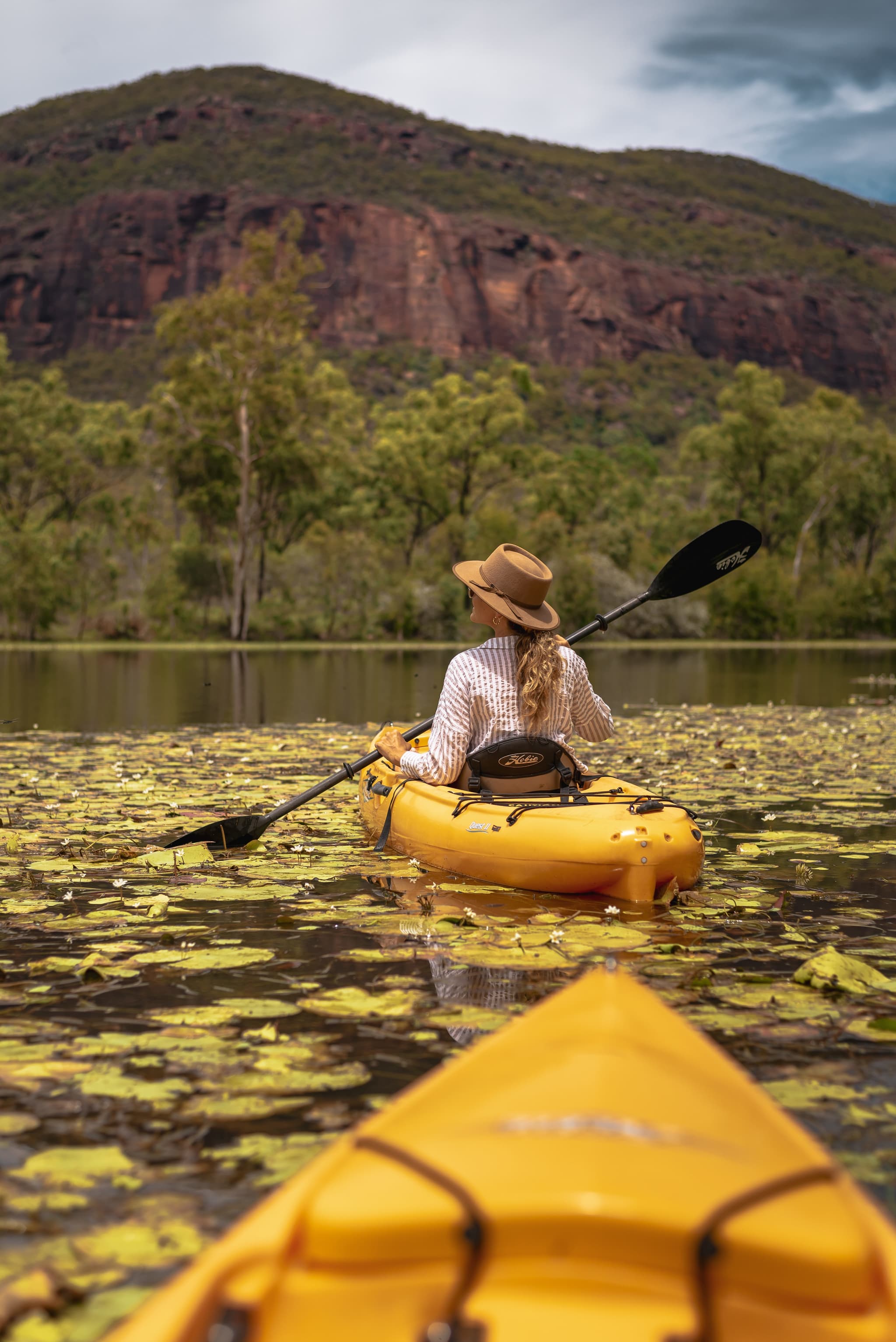 A person in a hat in a yellow kayak on a green lake