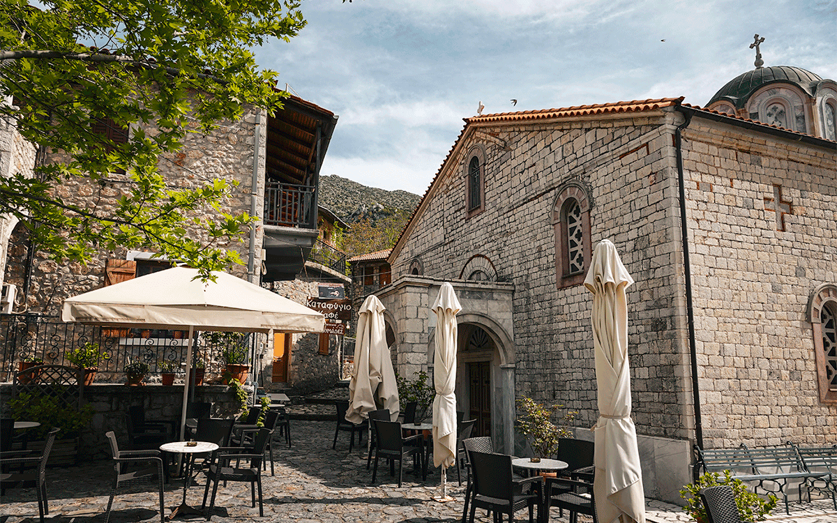 Outdoor cafe seating with church in the background in village of Lagkadia, Peloponnese, Greece