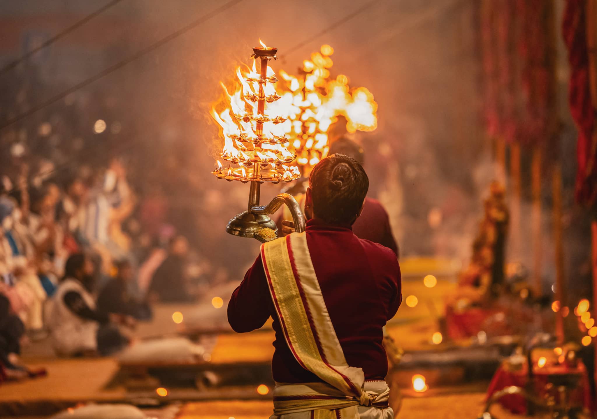 Priest performing traditional fire ritual in India during immersion cultural tour with vibrant flames and crowd watching.