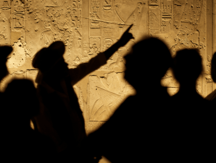 Silhouetted tour guide pointing at ancient Egyptian carvings, highlighting solar eclipse symbols on an Egypt tour.